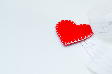 red felt heart on the background of a paper printout of an ECG chart or an electrocardiogram on a white background. Prevention of cardiovascular diseases..