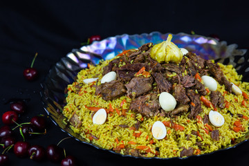Pilaf and ingredients on plate with oriental ornament on a black background. Central-Asian cuisine - Plov Top view