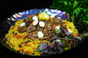 Pilaf and ingredients on plate with oriental ornament on a black background. Central-Asian cuisine - Plov Top view