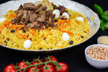 Pilaf and ingredients on plate with oriental ornament on a black background. Central-Asian cuisine - Plov Top view