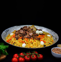 Pilaf and ingredients on plate with oriental ornament on a black background. Central-Asian cuisine - Plov Top view