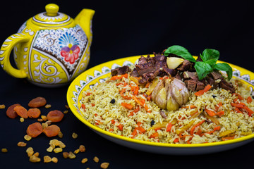 Pilaf and ingredients on plate with oriental ornament on a black background. Central-Asian cuisine - Plov Top view