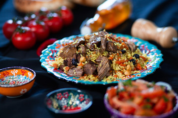 Pilaf and ingredients on plate with oriental ornament on a black background. Central-Asian cuisine - Plov Top view