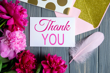 Peonies pink flowers on a gray wooden background with a mail envelope and the inscription thank...