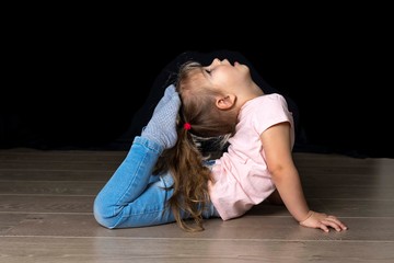 Fototapeta na wymiar Little girl does gymnastics in jeans on a black background in quarantine