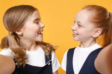 Two young little girls 12-13 years old in white t-shirt blue school uniform dresses isolated on yellow background children studio portrait Childhood kids education lifestyle concept Mock up copy space