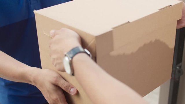 Young postal delivery courier man holding parcel boxes for sending to customer, Asian men signing and pay via qr code on mobile phone for receive delivered parcels outdoors.
