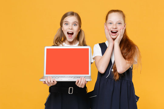 Two girls 12-13 years old white t-shirt blue school uniform hold laptop pc computer isolated on yellow background children studio portrait Childhood education lifestyle concept Mock up copy space wow