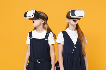 Two girls 12-13 years old in headset virtual vr reality t-shirt blue school uniform isolated on yellow background children studio portrait Childhood kids education lifestyle concept Mock up copy space