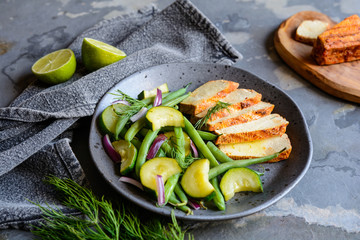 Marinated tofu slices served with blanched green beans and zucchini, drizzled with olive oil and decorated with fresh dill