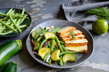 Marinated tofu slices served with blanched green beans and zucchini, drizzled with olive oil and decorated with fresh dill