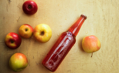 Background with a bottle of red cider and fresh apples that lie on the table.