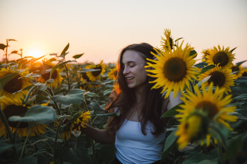 Young caucasian girl with long dark hair and white t-shirts in summer sunflower field, looking happy, summer concept, morning joy
