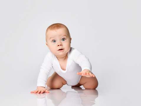 Chubby ginger baby boy in bodysuit, barefoot. He smiling, creeping on floor isolated on white background. Close up, copy space
