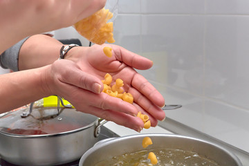 Mujer vertiendo la pasta de los macarrones en la cazuela con agua, aceite y laurel.