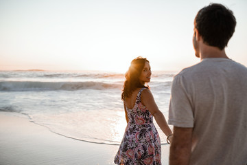 Young woman leading her husband to the ocean at sunset