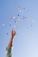 Hand throwing Colorful confetti in blue sky