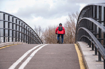 bicycle cyclist, a man in a red jacket, helmet and with a backpack traveling, moved along a bicycle path on a bridge
