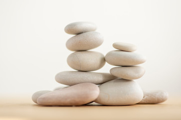 Fototapeta na wymiar Simplicity stones cairns isolated on white background, group of light gray pebbles built in towers, wood table