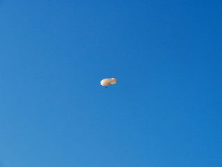 A large white airship flies in a bright blue sky. Summer day