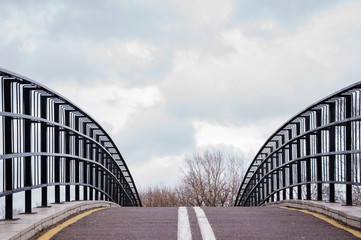 Double-sided bicycle path with markings runs along the bridge with iron sides and goes into the distance to the cloudy sky.