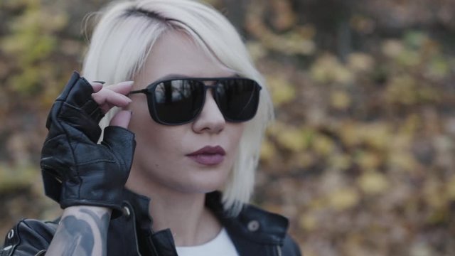 Portrait of female biker undresses sunglasses and looks in park