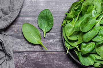 Fototapeta premium Fresh organic baby spinach leaves on a plate on dark wooden table top view. Healthy and organic food concept.