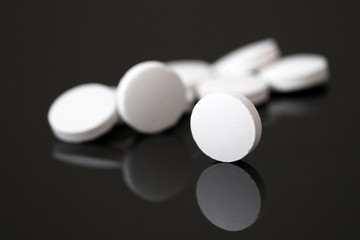 White pills are reflected in dark glass, tablets on black background. Concept of pharmacy, medication or vitamins