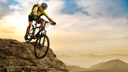 Fototapeta na wymiar Cyclist Riding the Bike Down the Rock at Sunrise in the Mountains. Extreme Sport and Enduro Biking Concept.