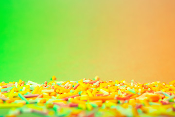 Cake decorating sweets, green and orange background, baking colorful sprinkles, home baking decorations, copy spce for text, bright colors, pile of sweets, multicolored sweet pieces