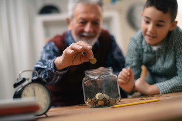 Grandpa and grandson saving money. Grandfather teaching grandchild how to save money.	