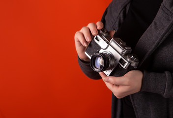 The vintage camera of the old model is in the hands of a girl. In the photo hands of the model and the camera on an orange background