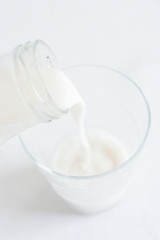 Minimal set of a glass bottle pouring white liquid milk in a glass, with white background