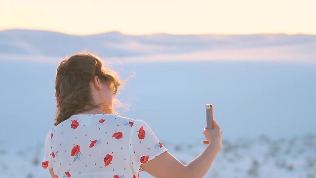 Slow motion of young woman girl closeup taking selfie picture in white sands dunes national monument in New Mexico using phone with wind hair