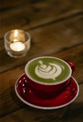 Obraz na płótnie Canvas Healthy red cup of matcha tea with foam and a candle light, on a wooden table with copy space on the top