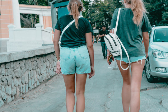 One of girls with very long legs wears too short jeans shorts another one wears classic shorts on waist. Un-self-conscious woman. Fashion. City. Urban. Open c young people. Youth. Summer. Hot