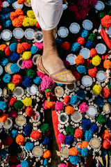 Obraz premium Foot of a man with a traditional Rajasthan shoe and a hand, on the top of a camel decorated with colorful pom pom decorations and rounded mirrors