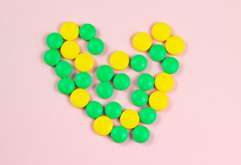 Green and yellow medical pills on a pink background.