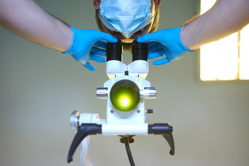 A medical scientist looks through a microscope. Medic in a protective mask with a microscope. Kovid-19. Medical research with a microscope in a laboratory. Сoronavirus vaccine search.