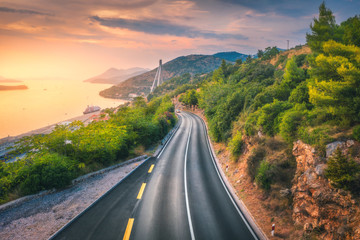 Aerial view of perfect mountain road and beautiful green forest at colorful sunset in summer. Dubrovnik, Croatia. Top view of road, sea, mountain, sky. Landscape with highway, sea coast, gold sunlight