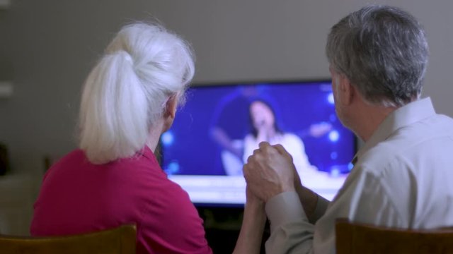 A mature couple worshiping as they attend virtual church by streaming the online platform to their television because congregation and group fellowship is restricted during COVID19 pandemic.