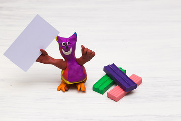 A plasticine figure resembling a cat on a light background holds a clean empty table. Blank sheet. Copy space
