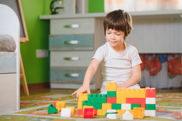 Child playing with colorful toy blocks. Little boy building tower at home or day care. Educational toys for young children. Construction block for baby or toddler kid. Mess in kindergarten play room.