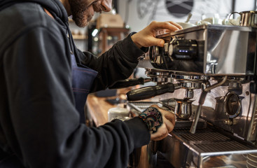 Cropped image, male barista using professional coffee machine enjoying job in cafe improving skills of making cappuccino