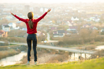 Fototapeta na wymiar Young woman standing outdoors raising her hands enjoying city view. Relaxing, freedom and wellness concept.