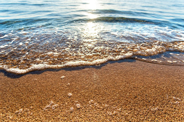Close up of small sea waves with clear blue water over yellow sand beach at summer sunny shore.