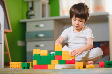 Adorable little boy playing with building cubes at home, laying on floor.