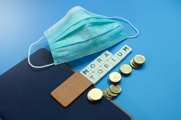 Surgical face mask, a notebook, block letters and stack of coins on blue background 