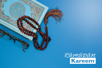 View of a Quran and prayer beads on blue background.  Religion and festive concept.