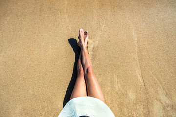Long slim young woman legs relaxing lying down and sunbathing on sand tropical beach under hot sun...